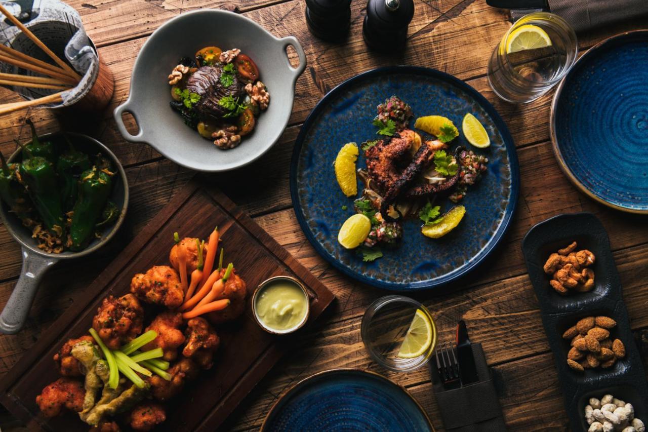 Five Jumeirah Village 두바이 외부 사진 The photo displays a beautifully arranged spread of various dishes on a wooden table. 

1. In the center, there's a blue plate featuring a main dish garnished with lemon slices and fresh herbs.
2. To the left, another dish includes fried pieces, like