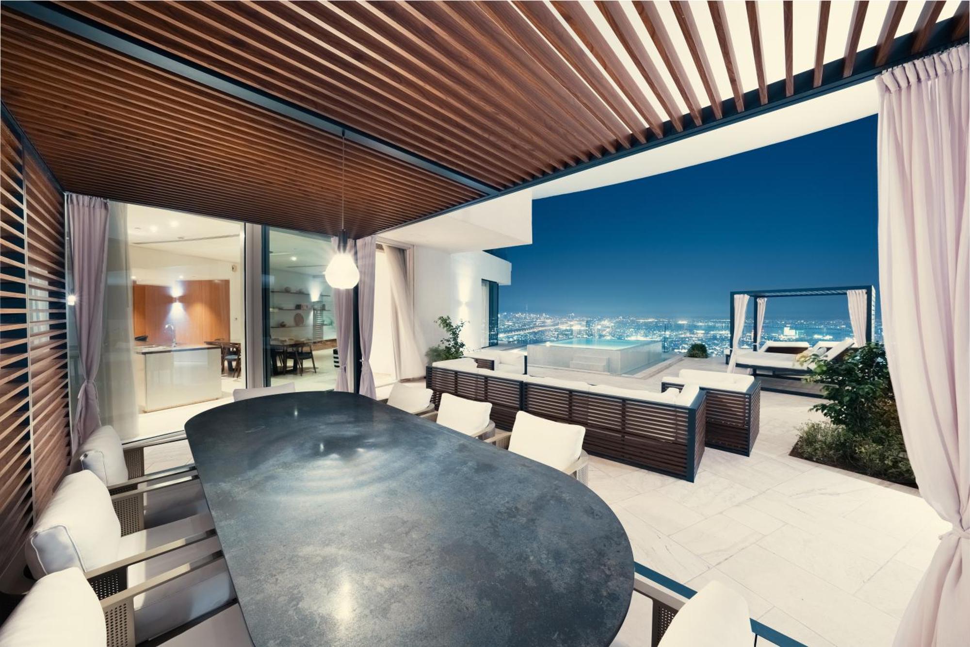 Five Jumeirah Village 두바이 외부 사진 The photo shows a modern outdoor dining area with a sleek, curved table surrounded by several chairs. It features a stylish wooden ceiling with slats, creating a shaded atmosphere. In the background, large glass doors lead to the interior of a house,