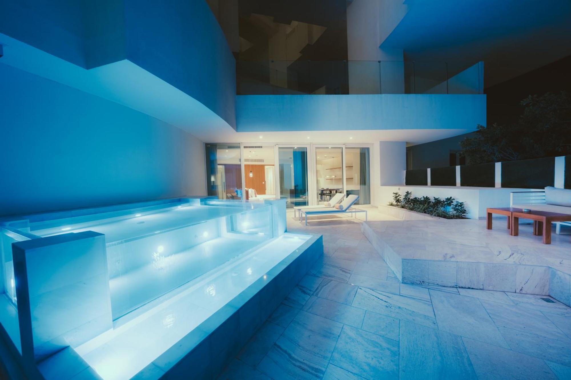 Five Jumeirah Village 두바이 외부 사진 The photo shows a modern outdoor area, likely part of a contemporary home. It features a stylish, illuminated staircase leading down to a pool or water feature, with soft blue lighting that creates a serene atmosphere. In the background, large glass 