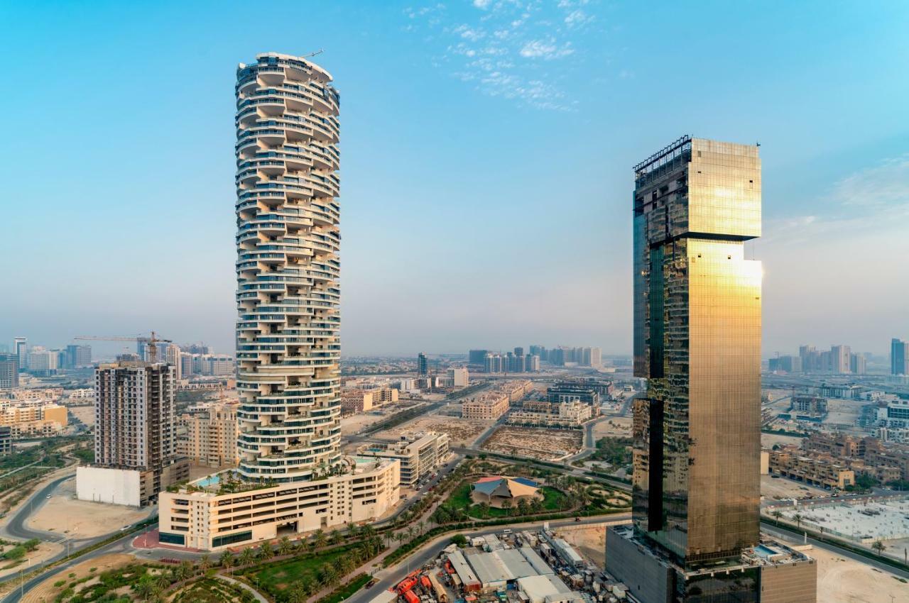 Five Jumeirah Village 두바이 외부 사진 The photo shows two distinctive skyscrapers located in an urban area. On the left, there is a tall, cylindrical building with a unique, modern design characterized by its twisting, spiral shape and balconies at various levels. To the right, there is 
